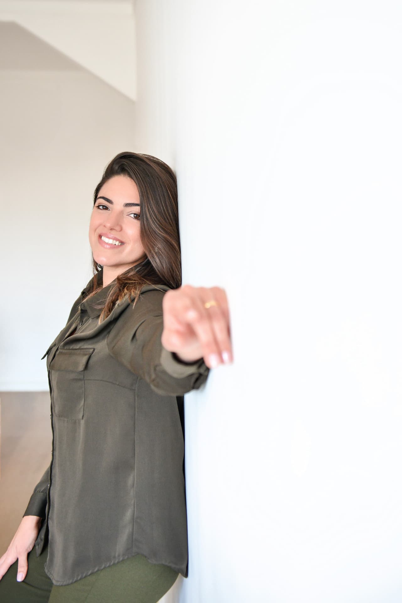 Jéssica Ferreira sorrindo apoiada em uma parede branca, apontando para a câmera
